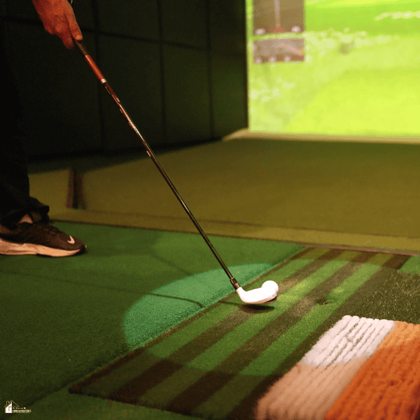 A person practices golf on artificial turf with an indoor simulator, showing an idea for transforming an unused room into a space for recreation.