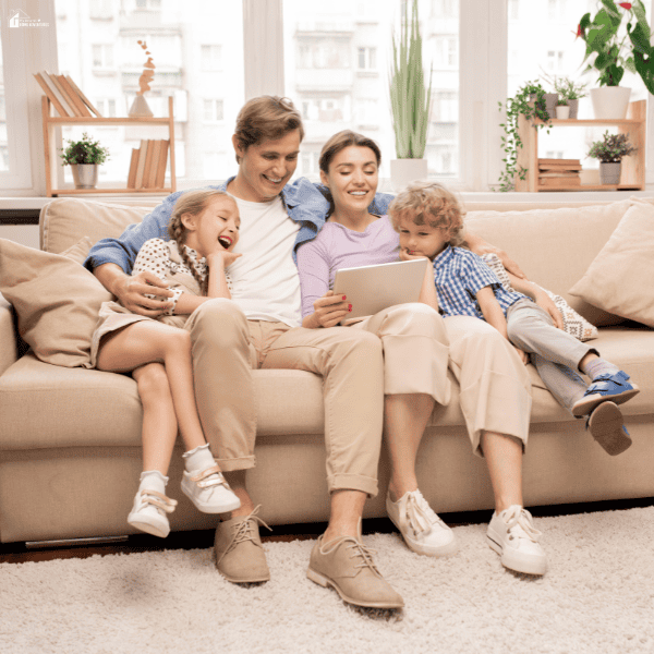Two parents and two children share a tablet on a beige sofa, illustrating how to turn an unused room into a space for relaxing together.