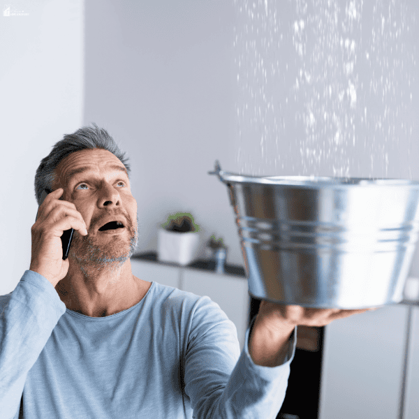 A man catches a ceiling leak in a metal bucket while calling for help, illustrating moisture problems that can lead to water damage and mold.