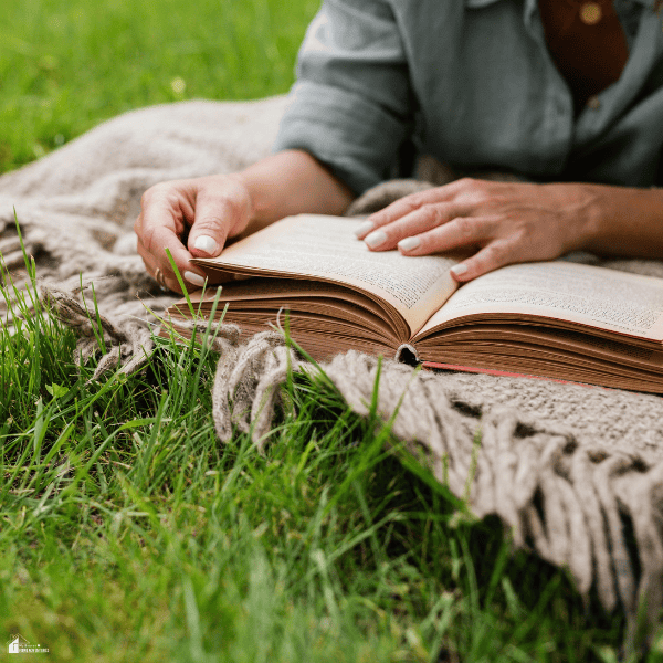 A person reads an open book on a textured, fringed outdoor rug, illustrating a comfortable rug setup for relaxing on grass.