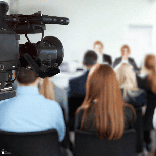 A video camera records speakers addressing an audience at a press event, illustrating the public communications work of a legit PR agency.
