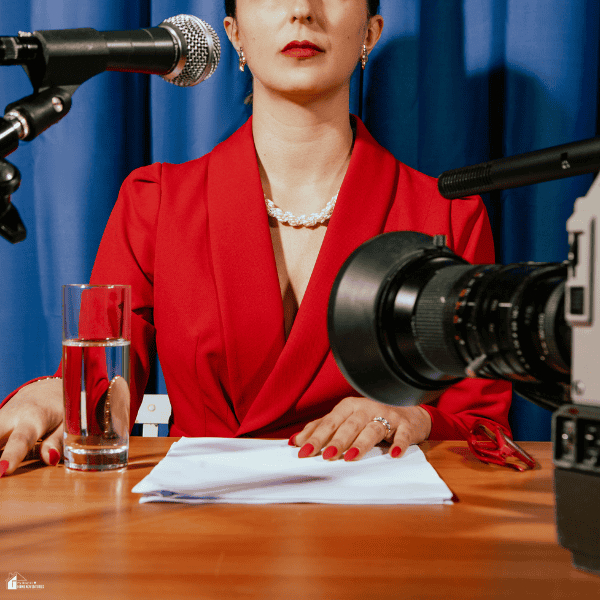 A woman in a red blazer faces microphones and a video camera, illustrating a press briefing relevant to a legit PR agency.