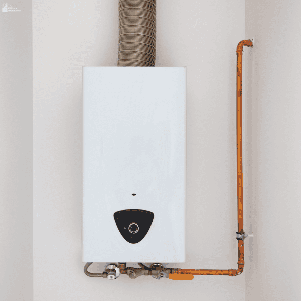 A white tankless water heater is mounted on a wall with copper pipes, control valves, and a metal exhaust duct.